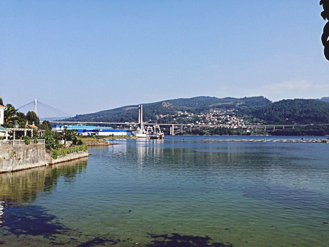 clear sky, water, copy space, built structure, architecture, blue, mountain, river, transportation, bridge - man made structure, connection, building exterior, waterfront, sea, mountain range, tranquil scene, nature, tranquility, scenics, outdoors