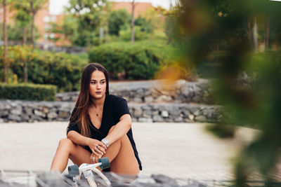 Young woman looking away while sitting on footpath