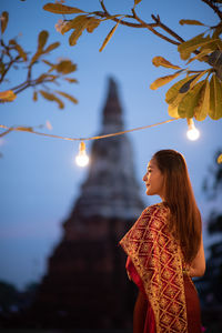 Woman wearing traditional clothing while standing against temple at dusk