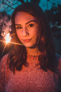Portrait of beautiful young woman standing against trees in park at night