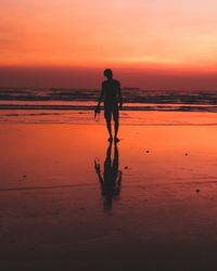 Silhouette man standing on shore at beach against sky during sunset