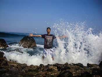 Waves splashing on rocks at shore against sky