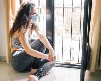 Young girl confinement with face mask at home looking out the window