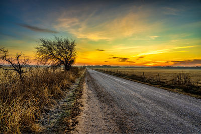 Road amidst field against sky during sunset