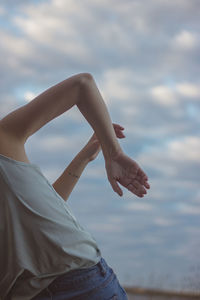 Midsection of woman dancing against cloudy sky