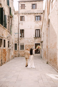 Rear view of newlywed couple walking amidst buildings