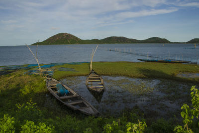 Boat moored on shore by lake against sky