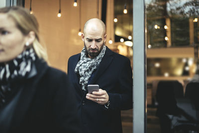 Mid adult businessman using mobile phone while leaving cafe