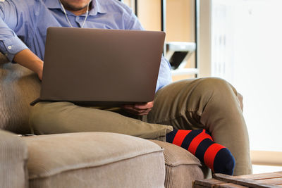 Midsection of man using laptop while sitting on sofa