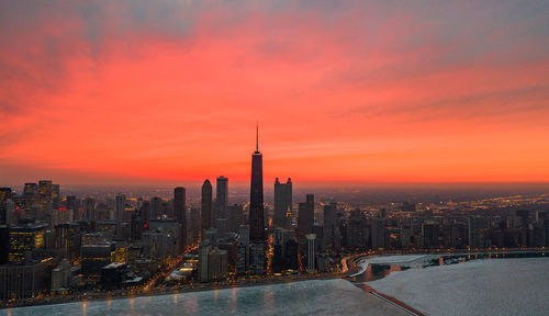 Aerial view of buildings by sea in city during sunset