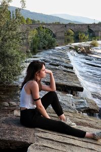 Side view of a smiling young woman sitting against plants