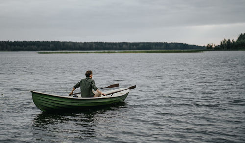 Man rowing while sitting in boat on lake against sky