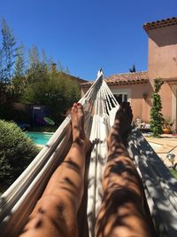 Low section of woman resting on hammock in yard against clear blue sky