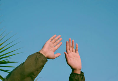 Low angle view of hands against blue sky