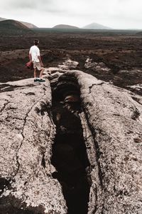 Rear view of woman on rock by landscape against sky