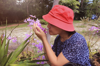 Young woman wearing hat smelling flowers at park