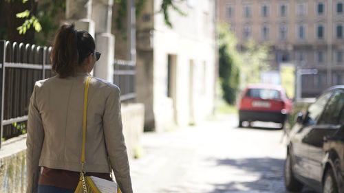 Rear view of woman walking on road along buildings