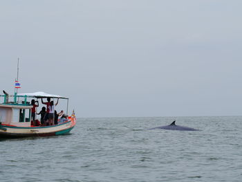 People sailing on boat by whale in sea against clear sky