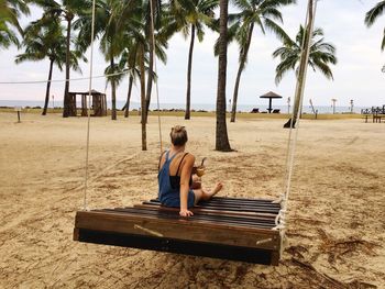 Rear view of woman sitting on wooden swing at beach