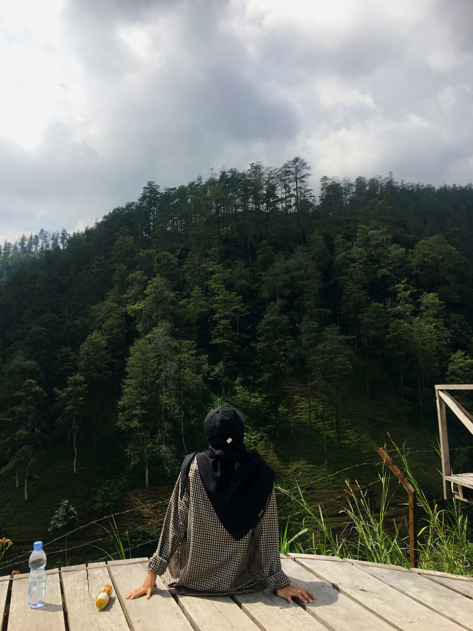 REAR VIEW OF WOMAN SITTING ON PLANTS AGAINST MOUNTAIN