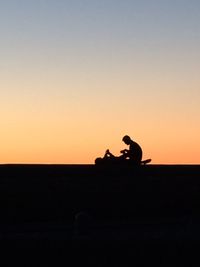 Silhouette man sitting against clear sky during sunset