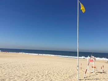 Flag on sand at beach against blue sky