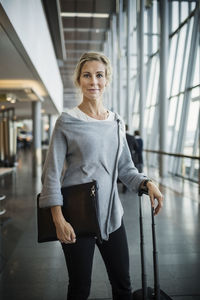 Portrait of confident businesswoman with luggage standing at airport