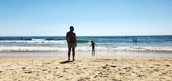 Rear view of men on beach against clear sky