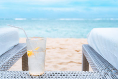 Close-up of drink on table at beach against cloudy sky