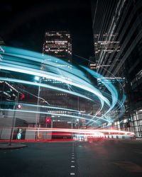 Light trails on road against illuminated buildings in city at night