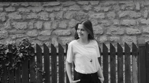 Portrait of young woman standing against brick wall