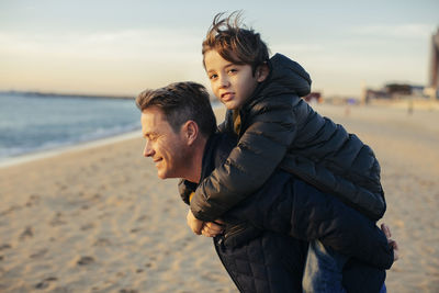 Portrait of father carrying son piggyback on the beach