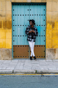 Portrait of woman standing on footpath against building