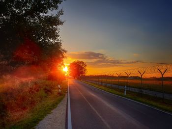 Empty road on field against sky at sunset