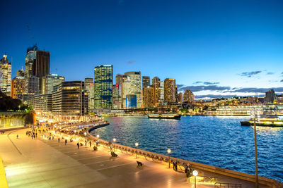 Illuminated modern buildings in city against clear blue sky