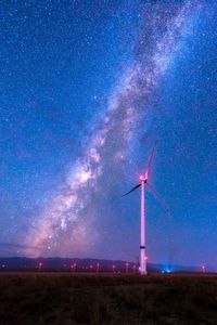 Wind turbines on field against sky at night