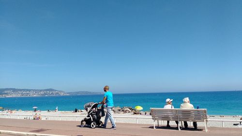 People sitting on beach against clear blue sky