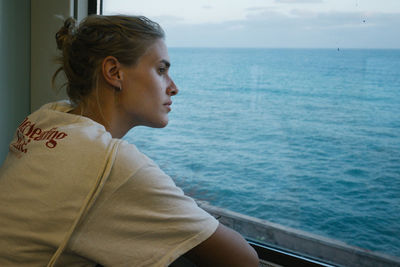 Young woman looking through window in boat against sea