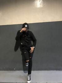 Full length of young man photographing while standing against wall