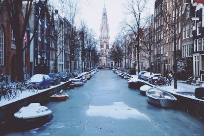 Boats in frozen canal amidst buildings in city during winter