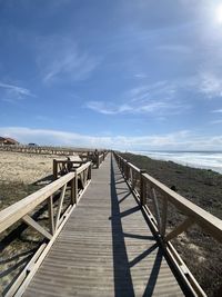 Boardwalk leading towards bridge against sky