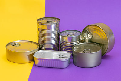 A group of stacked tin cans with blank edges on split yellow and violet background