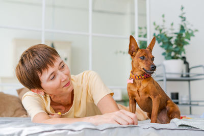 Mature woman lies on floor with slittle dog miniature pinscher