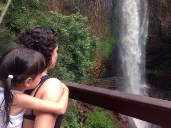 Mother piggybacking her daughter while looking at waterfall