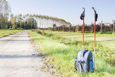 Backpack with hiking poles on field against sky