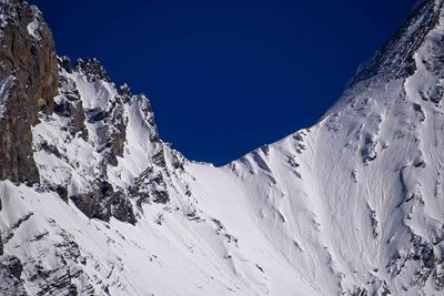 Low angle view of snowcapped mountains against clear blue sky