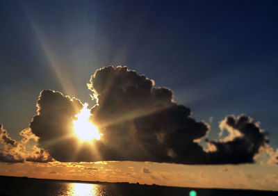 Low angle view of sunlight streaming through clouds during sunset