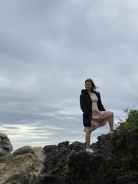 Full length of woman standing on rock against sky