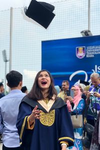 Cheerful woman in graduation gown throwing mortarboard 