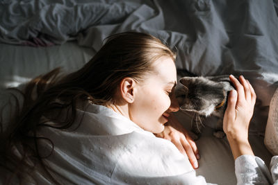 Candid portrait of young woman is resting with kitten on the bed at home one sunny day. girl play